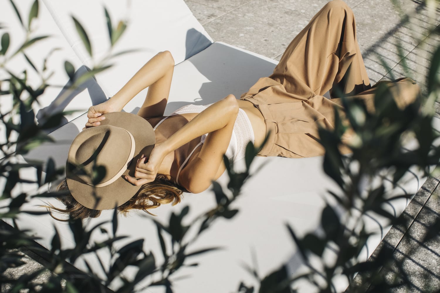 Mujer con sombrero tomando el sol en una tumbona rodeada por un árbol. 